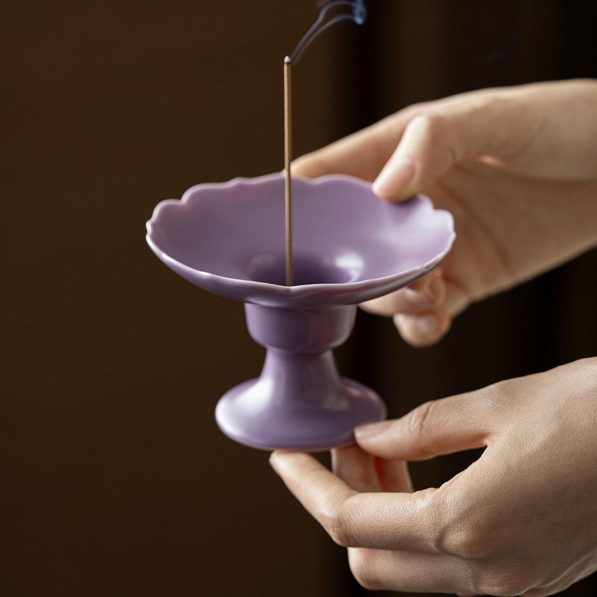 Ripple Footed Incense Dish in lavender Ru glaze held in two hands, incense stick burning