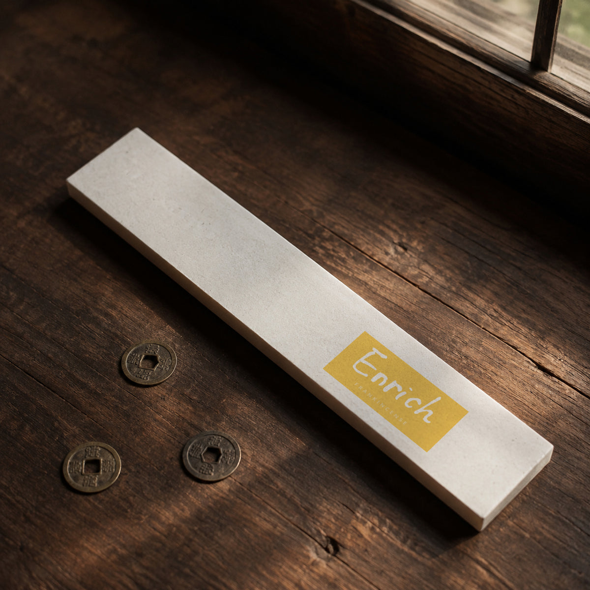 Enrich Frankincense Incense box beside three aged copper coins on a wooden table